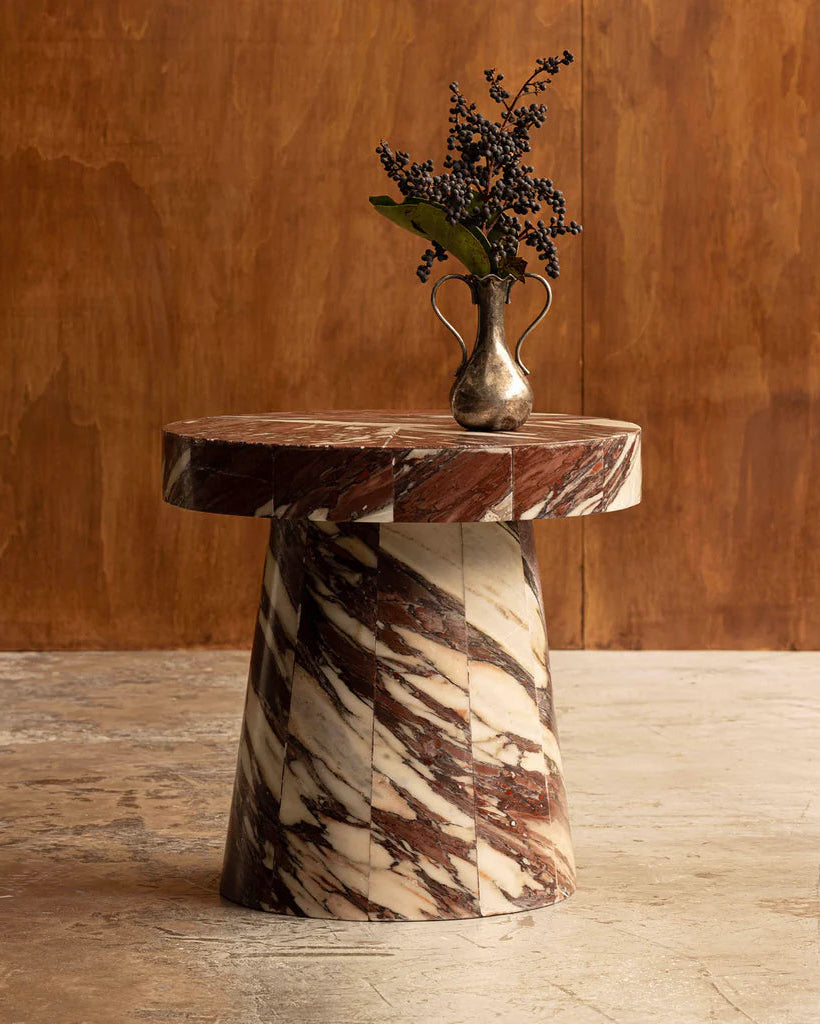Marble-patterned side table with a vase of flowers against a wooden wall.