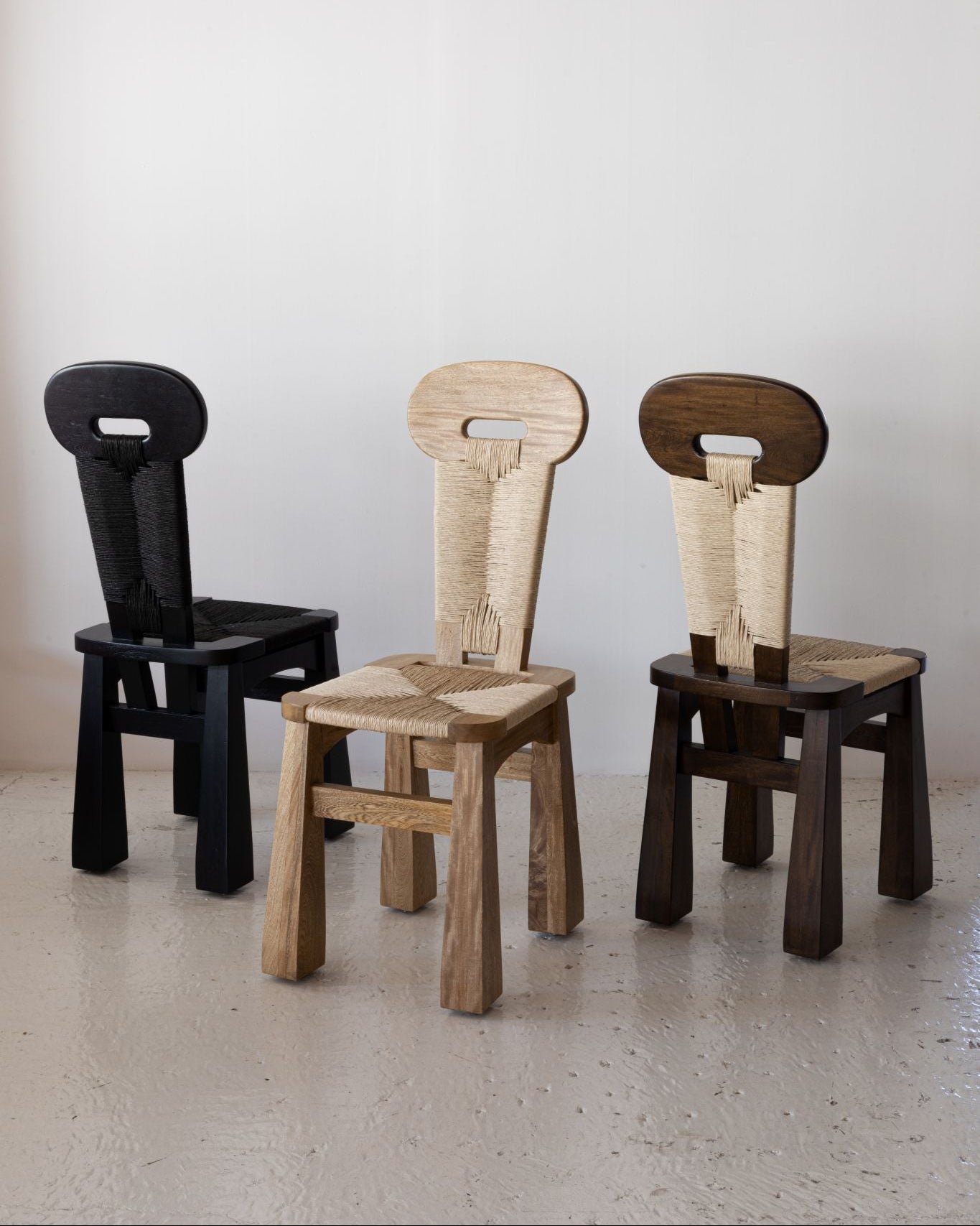 Three unique chairs in black, beige, and brown on a light floor with a white wall background.