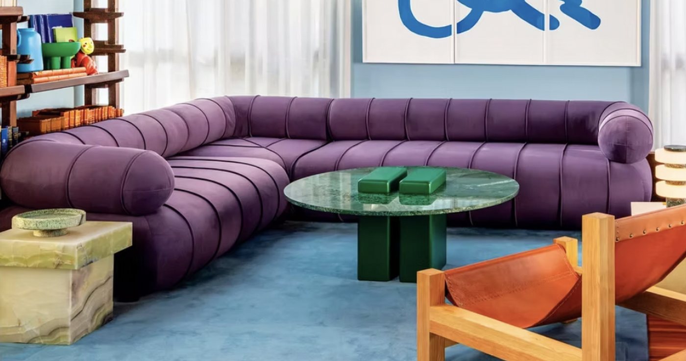 A showroom interior: a deep purple modular sofa, a round green marble table, a leather sling chair and a shelved wall of objects.